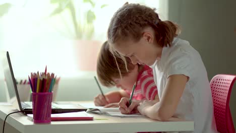 Educación-a-distancia-en-línea-de-los-niños-en-casa-utilizando-un-ordenador-portátil.-Hermana-y-hermano-están-escribiendo-en-cuadernos.-Brote-de-Coronavirus-Covid19.