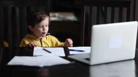 Kleiner-Junge-sitzt-am-Tisch-mit-Laptop-und-Dokumente-für-den-Unterricht-zu-Hause