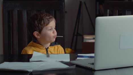 Niño-pequeño-se-alojó-en-la-mesa-con-computadora-portátil-y-documentos-para-la-lección-en-casa