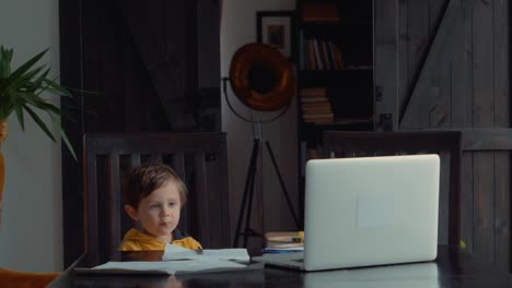 Niño-pequeño-se-alojó-en-la-mesa-con-computadora-portátil-y-documentos-para-la-lección-en-casa