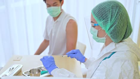 Female-doctor-take-syringe-equipment-give-vaccine-treatment-care-to-male-patient-check-up-for-covid-19-Corona-virus-in-clinic-hospital-room.-Wearing-glove-surgical-mask-and-face-shield-for-protection