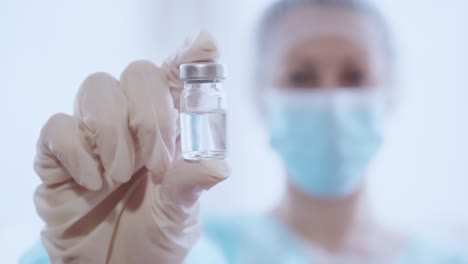 Mujer-doctora-en-uniforme-médico-sostiene-vacuna-vial-de-vidrio