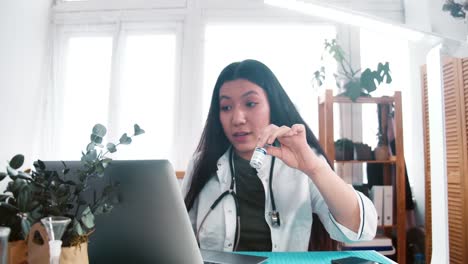 Zoom-in-professional-positive-multiethnic-doctor-woman-offers-vaccine-treatment-medication-to-remote-client-on-webcam.