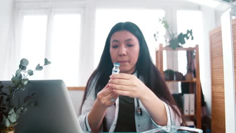 Vaccine-inspection.-Zoom-in-on-serious-young-multiethnic-pharmacy-doctor-woman-in-lab-coat-look-at-flask-with-medication