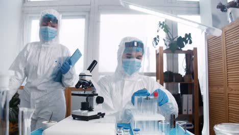 Focused-young-female-lab-scientist-doctor-in-full-medical-protection-suit-and-shield-works-on-new-coronavirus-vaccine.