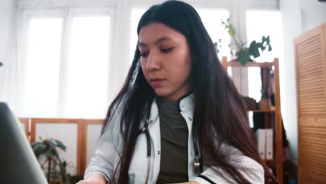 Zoom-in-on-serious-focused-young-multiethnic-pharmacy-doctor-woman-in-lab-coat-working-at-light-medical-clinic-office.