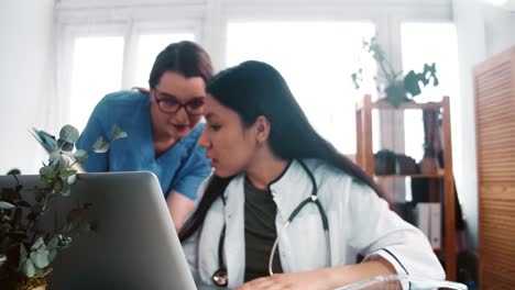 Junge-multiethnische-Apotheke-Arzt-Frau-Beratung-Remote-Client-auf-Laptop-Webcam,-im-Gespräch-mit-Assistent-in-blauer-Uniform.