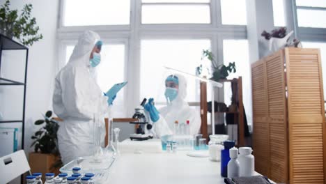 Creating-new-coronavirus-vaccine.-Professional-doctor,-scientist-woman-in-protection-suit-holds-cure-flask-at-clinic-lab