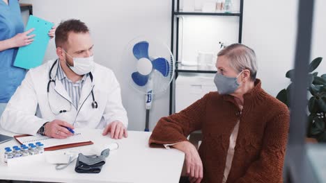 Joven-amable-médico-caucásico-en-bata-de-laboratorio-consultando-a-la-mujer-paciente-senior-en-la-oficina-moderna-del-hospital-de-la-clínica-ligera.