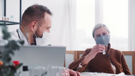 Un-médico-masculino-amigable-con-bata-de-laboratorio-ofrece-tratamiento-de-vacunación-a-la-paciente-mayor-feliz-en-la-oficina-del-hospital-de-la-clínica.