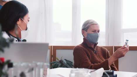 La-doctora-le-da-un-frasco-de-medicina-vacunal-a-una-mujer-cliente-principal-caucásica-sonriente-en-el-examen-médico-del-consultorio-de-la-clínica-ligera.