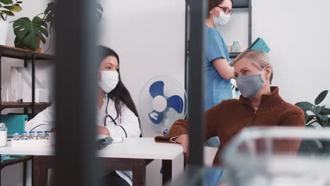 Joven-amigable-doctora-multiétnica-en-bata-de-laboratorio-consultando-a-la-mujer-paciente-senior,-sonriendo-en-la-oficina-del-hospital-de-la-clínica.