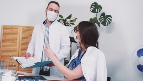 New-vaccine-concept.-Young-pretty-Caucasian-female-doctor-shows-cure-flask-to-male-colleague-at-light-clinic-office.