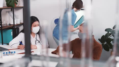 Joven-amigable-profesional-de-la-salud-multiétnica-en-el-laboratorio-de-abrigo-médico-consultando-a-la-mujer-cliente-de-pelo-gris-senior