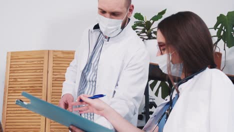 Young-Caucasian-female-pharmacy-doctor-signs-papers-for-male-colleague,-gives-flask-with-vaccine-at-light-clinic-office.