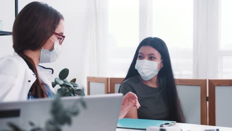 Young-friendly-Caucasian-physician-woman-in-lab-coat-consults-worried-mixed-race-patient,-takes-file-from-colleague.