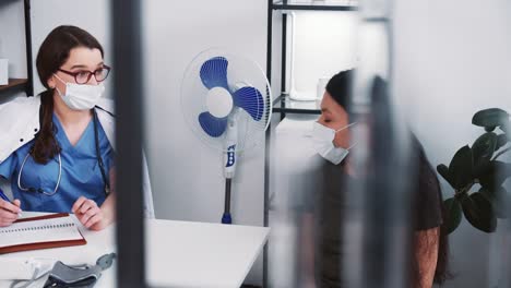 Medical-exam-concept.-Young-happy-friendly-female-physician-in-lab-coat-consulting-mixed-race-client-woman-in-face-mask.