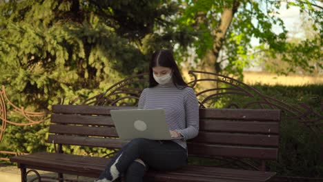 Frau-in-medizinischeSchutzmaske-Freelancer-arbeiten-mit-Laptop-im-Freien-im-Park