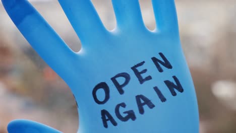 Blown-up-blue-latex-surgical-glove-on-black-background.-Reopening-covid-safe.-Open-again-text-written-on-medical-glove.-New-normal