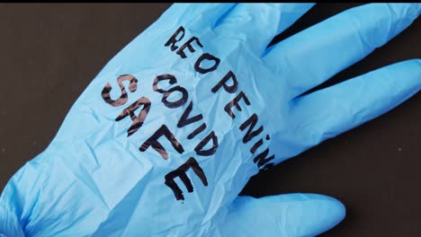 Blown-up-blue-latex-surgical-glove-on-black-background.-Reopening-covid-safe.-Open-again-text-written-on-medical-glove.-New-normal