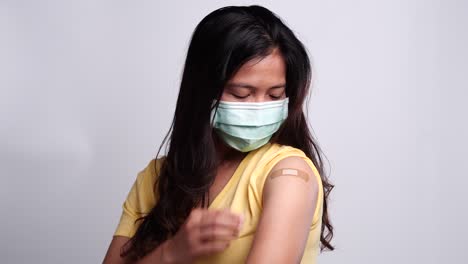 Woman-wearing-medical-face-mask-showing-her-arm-after-getting-vaccinated-with-feeling-happy.-Concept-of-vaccination,-vaccinated-patient,-vaccine-roll-out-program,-Coronavirus,-COVID-19.