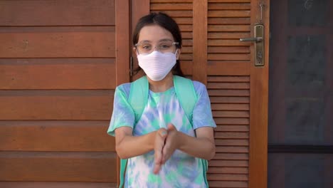 Little-girl-getting-ready-fot-school-using-hand-sanitizer-and-protective-face-mask-during-Covid-19.