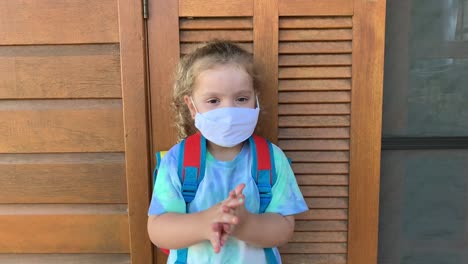Little-girl-getting-ready-fot-school-using-hand-sanitizer-and-protective-face-mask-during-Covid-19.