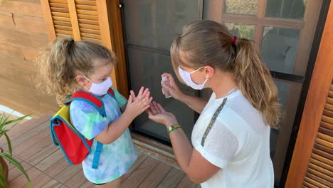 Little-girl-and-mother-getting-ready-fot-school-using-hand-sanitizer-and-protective-face-mask-during-Covid-19.