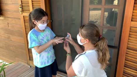 Little-girl-and-mother-getting-ready-fot-school-using-hand-sanitizer-and-protective-face-mask-during-Covid-19.