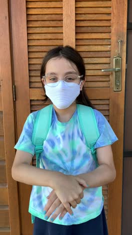 Little-girl-getting-ready-fot-school-using-hand-sanitizer-and-protective-face-mask-during-Covid-19.-Vertical-format-video