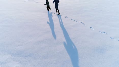 Mom-and-sun-are-running-together-in-snow.-Aerial-footage.-Family-pastime-in-winter.