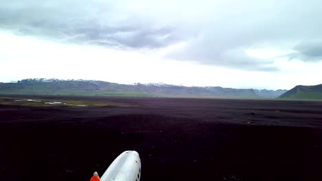 Mujer-joven-está-parado-brazos-extendidos-en-avión-que-se-estrelló-en-la-playa-de-arena-negra-mirando-su-contemplación-lugar-famoso-entorno-para-visitar-en-Islandia-y-posan-junto-a-los-restos-del-naufragio-4K-video