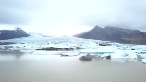 Vista-aérea-DRONE-de-mujer-contemplando-la-laguna-glaciar-en-la-situación-de-Islandia-en-la-orilla-del-lago