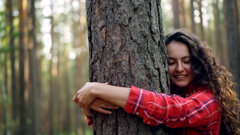 Schöne-junge-Frau-mit-lockigem-Haar-helles-Hemd-ist-Baum-Natur-genießen-und-mit-geschlossenen-Augen-lächelnd-umarmen.-Menschen,-Erholung-und-Freude-Konzept.