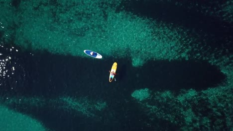 Video-from-above,-aerial-view-of--two-people-on-a-stand-up-paddle-(SUP)-in-Sardinia,-Italy.