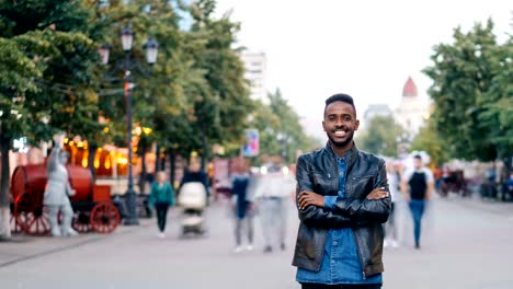 Zeitraffer-Porträt-von-gutaussehenden-Mann-afroamerikanische-Studenten-Blick-in-die-Kamera-und-lächelnd-ansehen-in-der-Straße-Downlown,-während-Menschen-um-ihn-herum-sausen-sind.