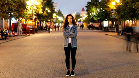 Time-lapse-de-mujer-atractiva-con-el-pelo-largo-y-rizado-permanente-en-la-calle-con-los-brazos-cruzados-y-mirando-a-cámara-el-otoño-por-la-tarde-cuando-las-personas-están-moviendo-alrededor.