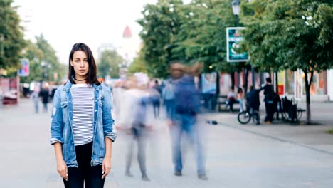 Time-lapse-de-la-infeliz-niña-solitaria-solas-en-la-calle-y-mirando-a-cámara-cuando-la-gente-está-caminando-alrededor-de-rápido.-Soledad-y-concepto-de-la-vida-moderna.