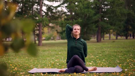 Fröhliche-Dame-übt-sich-im-Park-beim-Outdoor-Training-im-Stadtpark-in-Kuh-Gesicht-Pose-mit-Arme-hinter-dem-Rücken-sitzen.-Gesundheit,-Natur-und-Millennials-Konzept.