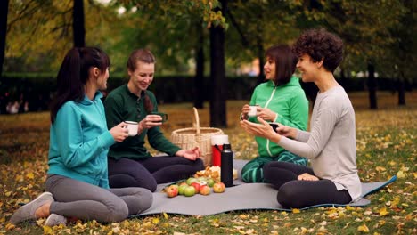 Glückliche-Mädchen-im-Park-sitzen-auf-Yoga-Matten-und-Essen-nach-dem-Outdoor-Training-im-Herbst-Picknick,-Mädchen-reden-lachen-und.-Kommunikation-und-Food-Konzept.