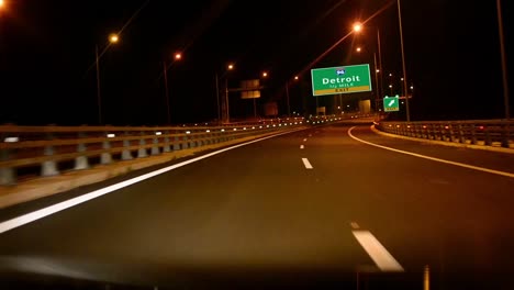 Por-la-carretera/la-autopista-en-la-noche,-señal-de-salida-de-la-ciudad-de-Detroit,-Michigan