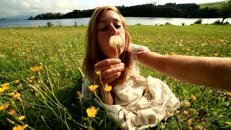 Female-takes-selfie-portrait-while-blowing-flower's-seeds-in-meadow