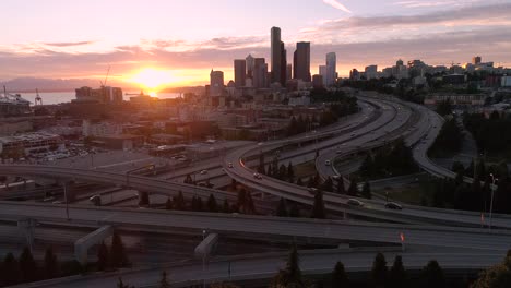 Drohne-Schuss-von-Seattle-mit-epischen-glühenden-Sonnenuntergang-auf-Autobahn-und-Innenstadt-Wolkenkratzer-Gebäude-in-der-Skyline-der-Stadt