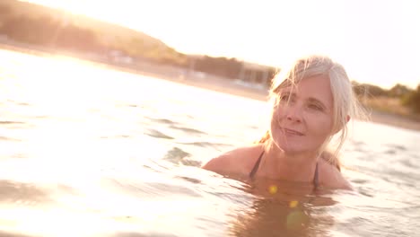 Mujer-senior-activa-nadando-en-el-mar-al-atardecer