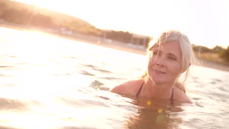 Active-senior-woman-swimming-in-the-sea-at-sunset