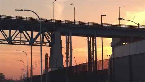 CLOSE-UP:-Silhouetted-cars-and-trucks-driving-through-industrial-town-at-sunset