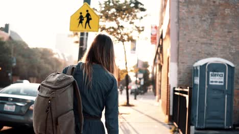 Back-view-of-young-stylish-woman-with-backpack-walking-alone-on-sunset-in-summer,-spending-time-in-downtown