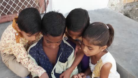 Indian-Kids-busy-on-a-touchscreen-tablet,-elder-sibling-teaching-them,-close-up-handheld