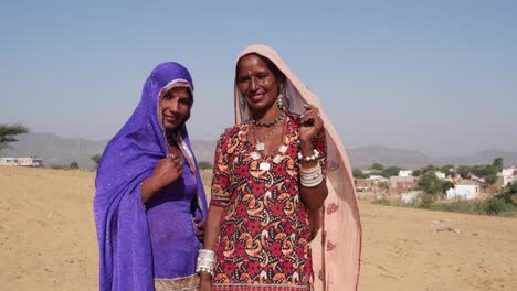 Pan-izquierda-a-dos-amigas-en-vestidos-tradicionales-de-Rajasthani-divirtiéndose-y-mirando-a-la-cámara