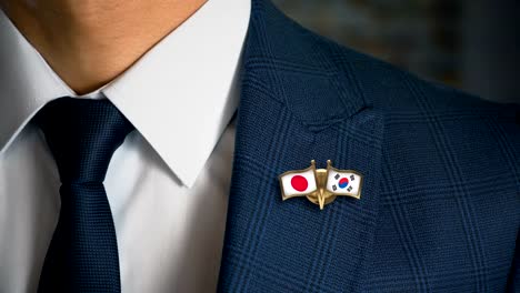 Geschäftsmann-zu-Fuß-in-Richtung-Kamera-mit-Freund-Land-Flaggen-Pin-Japan---Südkorea